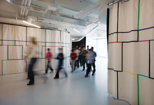 To control light levels and define classroom areas in the education center—with its separate student entry—the architects installed a sinuous ceiling-mounted track, along which runs a curtain designed by textile-artist Cindy Sirko.
