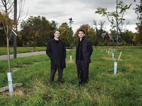 The two architects stand amid newly planted trees in a stormwater-infiltration forest at Detroit’s Latham Park. 