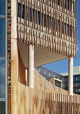 The Census Bureau building is clad in a brise soleil of wavy, laminated wood fins that are attached to a glass curtain wall, interrupted by concrete spandrels. The fins extend past the edges of the walls, creating a sinuous skin that breaks the box and enlivens the site.