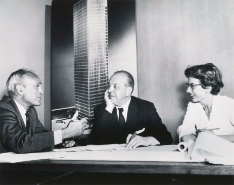 Philip Johnson, Ludwig Mies van Der Rohe, and Phyllis Lambert discuss the Seagram in front of an image of the building model soon after she helped the architects win the commission in 1955.