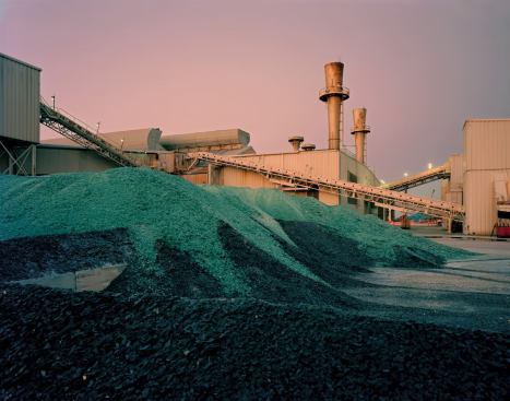 Broken glass to be recycled piles up at the mixing or "batching" end of PPG's float-glass factory in Wichita Falls, Texas. Conveyors in the background carry sand and other materials from storage to the plant's furnaces.