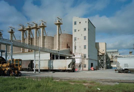 Then they travel, by a different conveyor belt, to the main factory building (the gray structure visible in the background), then enter the melter.