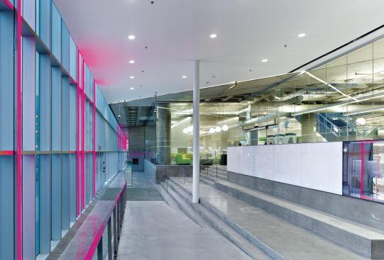 Color-changing LED fixtures are affixed to the inside of the curtainwall. The light reflects back into the library entrance vestibule. The ground floor is actually slightly above grade, and accessed by concrete ramps and stairs; a glass wall by the stairs has a holographic film that allows it to double as a projection screen.