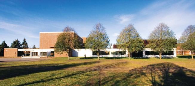 The expanded arts center extends the architectural edge along the campus mall, with white stucco walls and ribbon windows that continue the language established by Curt Green's auditorium entrance (at left in photo).