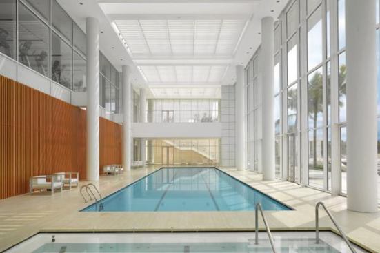 The fitness center’s indoor pool is lined with a cherry wood screen wall and windows that open into a solarium (at rear) and spa (at left). A skylight shaded by fixed aluminum screens brings light into the double-height space, as does a glazed wall that looks out at the outdoor pool.