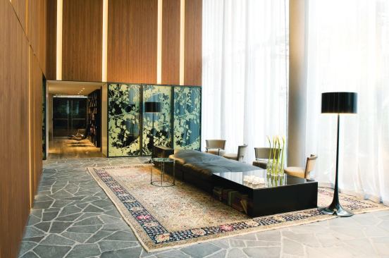 Designed by Antonio Citterio and Partners, the hotel lobby contrasts natural materials such as warm wood paneling and slate floors with bold, graphic elements. An abstract foliage pattern can be seen on lobby and elevator walls, and an eclectic modern aesthetic is achieved by pairing sleek custom furniture with Oriental rugs.