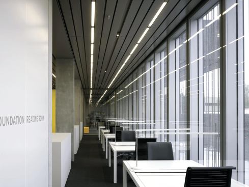 Several public areas are placed along the glazed perimeter walls, including this reading room that provides a place for scholars and the general public alike to examine documents including maps and photographs from the museum's library and archive. Metal ceiling panels and light fixtures create a linearity that runs perpendicular to the patterning on the glazing.