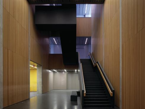 The linear motif of the building is carried through to the staircase, which, placed against the existing building, serves as a new central core for the building complex. But instead of featuring visually cool materials of glass or metal, this space is characterized by warm wood wall panels.