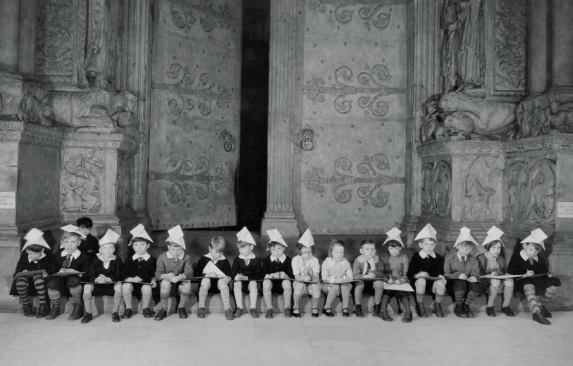 Wearing paper hats, a class of elementary-school students sits in front of the cast of the St. Gilles abbey for an art lesson in 1924. 