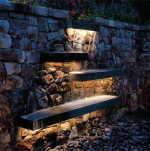 High-output white LED striplights are tucked on the underside of cantilevered flagstone slabs to illuminate this waterfall feature in a suburban backyard garden.