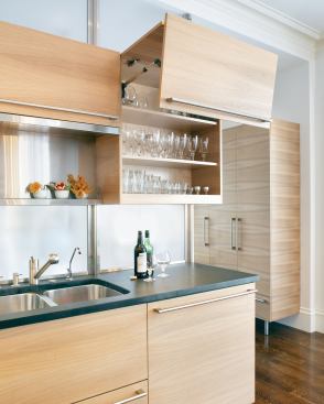 Vertically hinged upper doors align with the drawer layout below. A translucent screen of etched glass panels defines an adjacent entry/mudroom, where an armoirelike coat closet provides a visual link back to the kitchen.