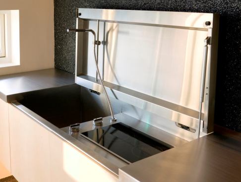 The stainless steel countertop along the room’s textured stone wall lifts to reveal a recessed sink and cooktop.