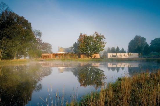 The new linear house, built behind the stone cottage, relates to the old fieldstone walls and a new pond.

