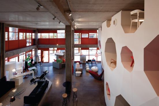 The program of the Orange Cube is purely commercial: The ground floor and mezzanine level are occupied by furniture retailer RBC, topped by five levels of office space. On the ground floor and mezzanine, furniture is displayed in wall units that feature voids similar to the ones that cut through the building structure.

