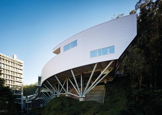 The building is elevated above the sloped and curving site on a system of steel support members and seismic base isolators.