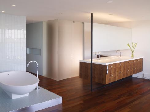A two-sided peninsula emerges from the west wall, its mirror and its floating, figured-walnut cabinet supported by a slender, straplike column of gun-blue steel.