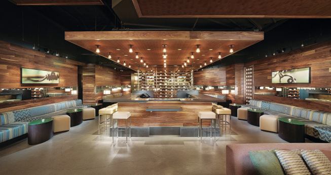 The tapas bar is the only place where wines from multiple wineries can be purchased. Framed by custom banquettes and with an events lounge tucked behind a wall-sized wine rack, this, the third of three main bar areas, is kept quiet enough for conversation with acoustic fabric lining the unfinished ceiling above the decorative soffits. BANQUETTE FABRIC - Maharam - Repeat Classic fabric - maharam.com - DECORATIVE LIGHT FIXTURES - Resolute - Clarity Ceiling fi xtures - resoluteusa.com - STOOL AND OTTOMAN UPHOLSTERY FABRIC - Architex - Voila upholstery fabric in Mushroom - architex-ljh.com - BARSTOOLS - ISA International - 1292 Cube barstool - haveaseat.com - TRACK LIGHTING - Translite Sonoma - Micro Spot G - translite.com
