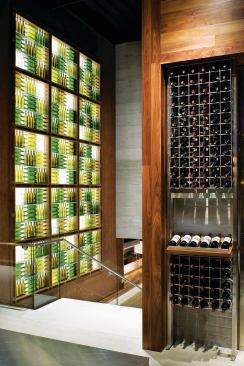 Empty wine bottles backlit by LED fixtures form a sculptural feature wall at the top of the main staircase that leads to the tasting bars. The empty bottles are complemented by full ones in the nearby retail display, which was designed and fabricated by Eclipse Designs. WALLCOVERING - Jelinek Cork Group - Fabric Cork - jelinek.com - WALL SURFACING - Giampolini & Co. - Boardformed cement plaster - giampolini.com - DISPLAY LIGHTING - Winona LED - LED display lighting - winonalighting.com