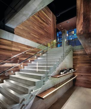 The main staircase provides access from the ground-floor reception/retail space down to the tasting and tapas areas of Press Club. Walnut shelves (with inset LED strips to light the labels) showcase some of the bottles that can be tasted at the different winery stations. STEP LIGHTS - Winona LED - Step 02 Square Deco step lights - winonalighting.com - WOOD PANELING - Plant Architectural Woodwork - American black walnut - plantwoodwork.com - STAIR RAIL ASSEMBLY - Eclipse Design - Custom stainless steel and glass stair rail - eclipsedesigngp.com