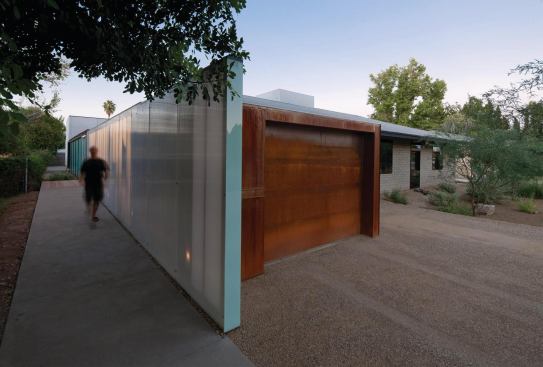 The garage's rusted steel facing and door contrast with the smooth polycarbonate panels of the garden wall.