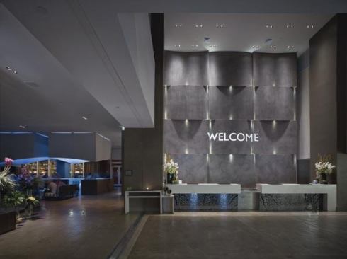 Small LED pointlights are embedded in the concrete wall behind the first floor lobby registration area. Small aperture downlights provide additional accent lighting and illumination for the desk surface.