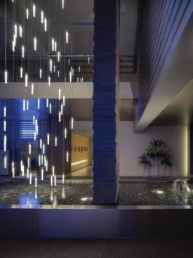 At the elevator banks in the background, backlit resin bands emit a saturated blue light and serve as indicator lights for the elevators. As the elevators move the light changes from white—an indicator of the cab’s location—to blue.